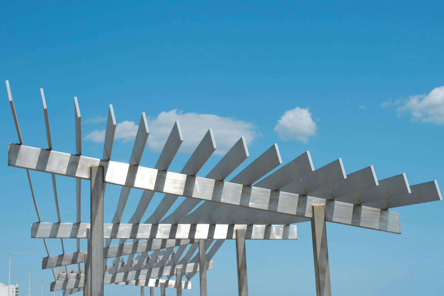 Pergola moderna in metallo con travi orizzontali sotto un cielo limpido.