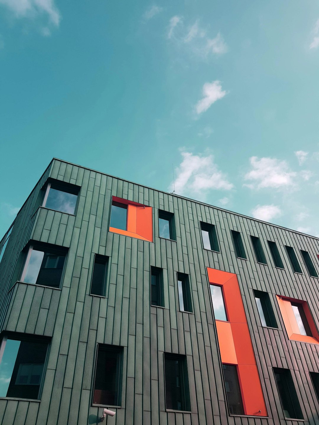 Facciata di un edificio moderno con pannelli metallici e accenti rosso-arancio.